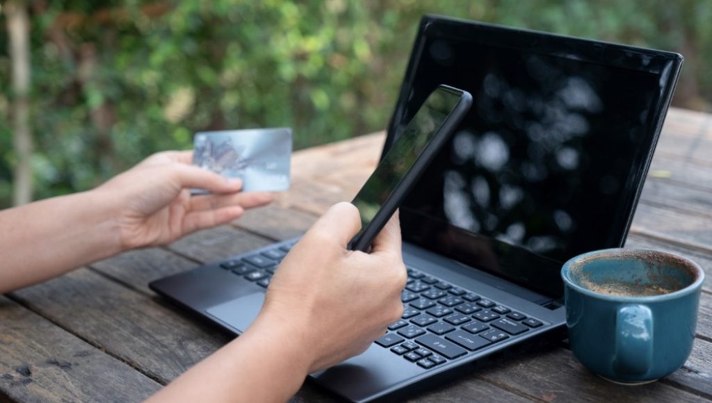 Smartphone and credit cards in hand with laptop 