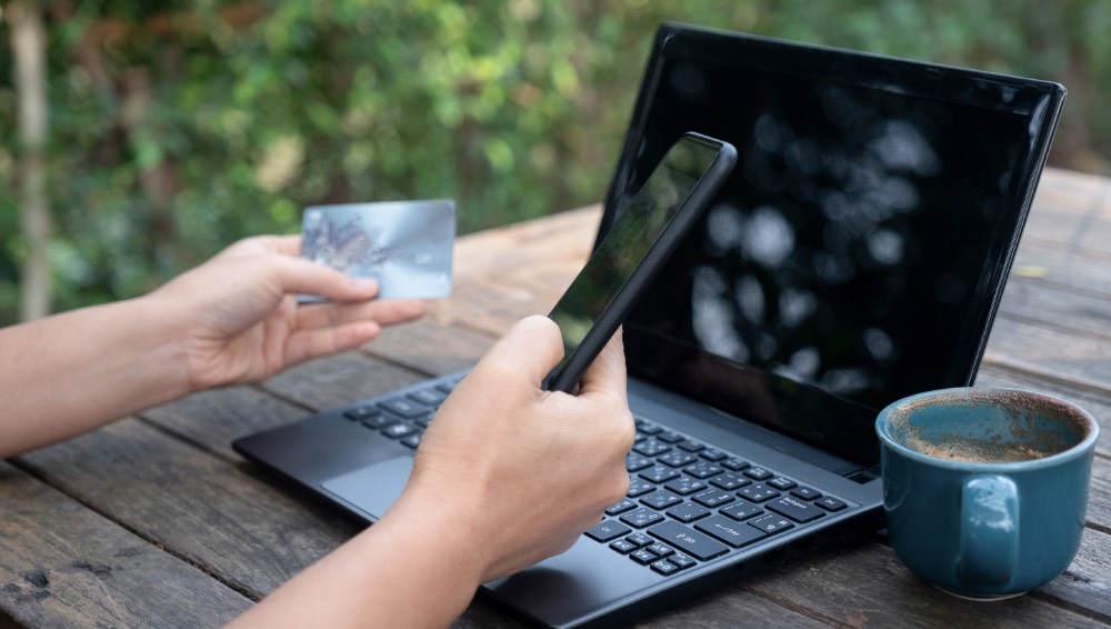 Smartphone and credit cards in hand with laptop
